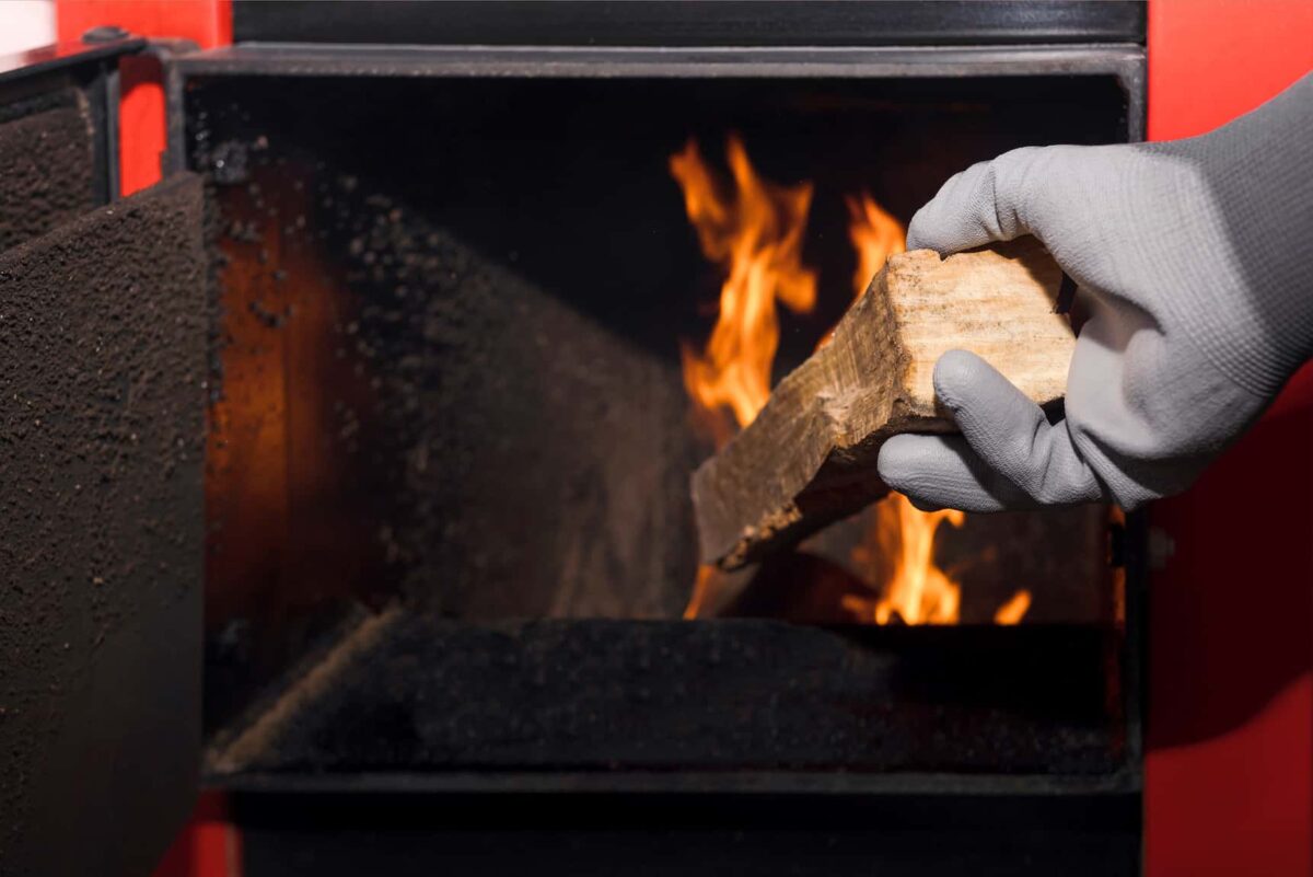 Image d'une personne plaçant une bûche de bois dans une chaudière à bois enflammée.