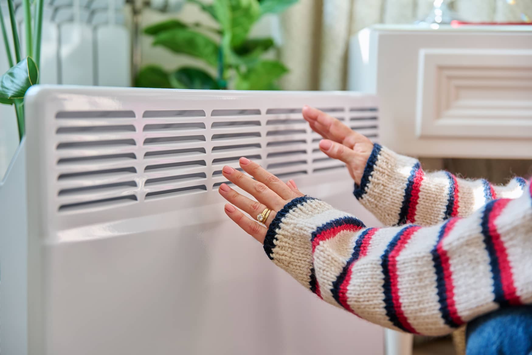 Personne réchauffant ses mains près d'un radiateur électrique moderne dans une maison confortable.