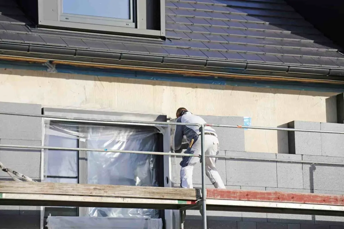 Ouvrier installant des panneaux isolants sur les murs extérieurs d'une maison pour une meilleure isolation thermique