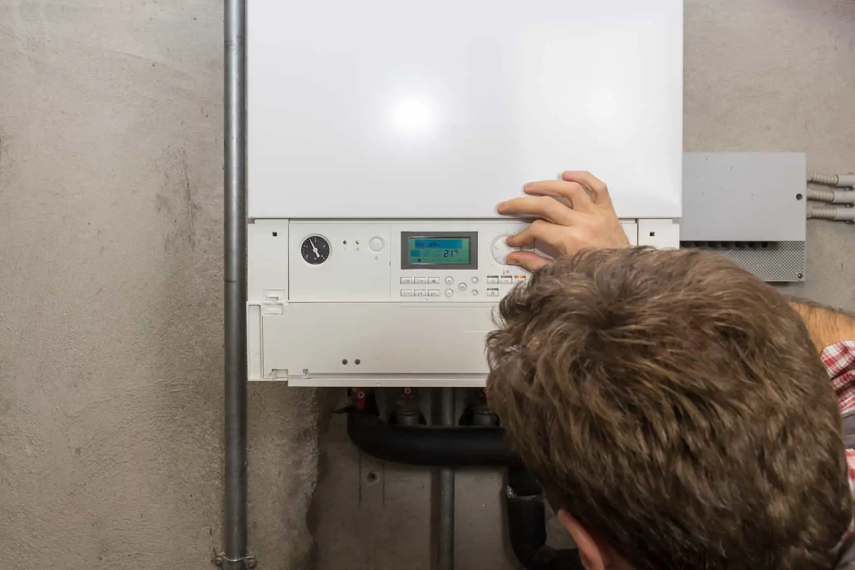 Technicien ajustant les paramètres d'une chaudière à condensation dans une maison, assurant le bon fonctionnement et l'efficacité du chauffage.