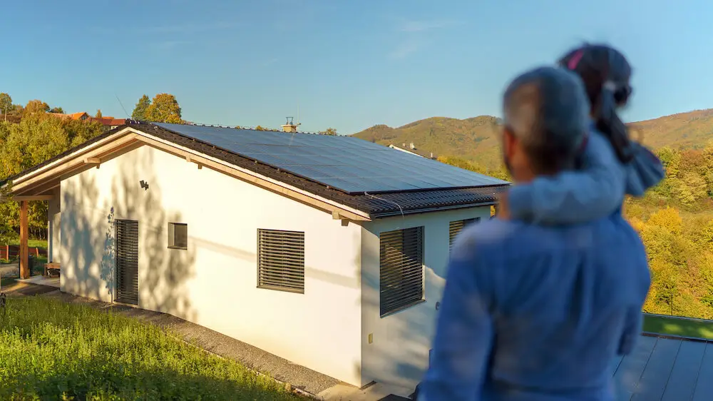 Maison rénovée avec panneaux solaires sur le toit, parent avec enfant observant la propriété. Solutions écologiques pour l'efficacité énergétique et autoconsommation.